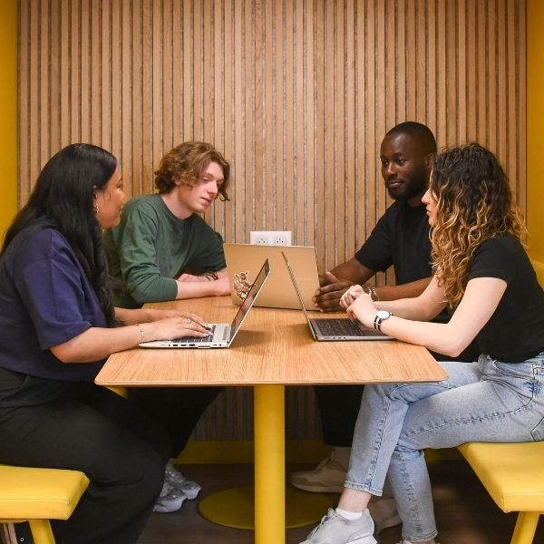 Groupe de quatre étudiants assis autour d'une table face à leurs ordinateurs
