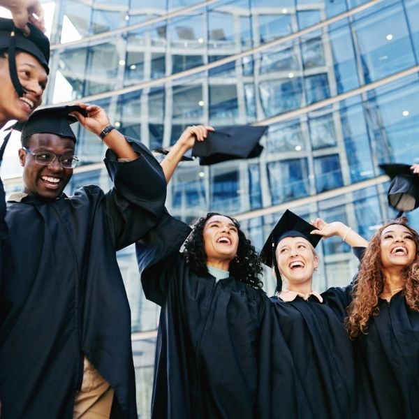 Etudiants à leur remise de diplôme Etudiants en toge jetant leur chapeau à leur remise de diplôme avec des bâtiments en fond