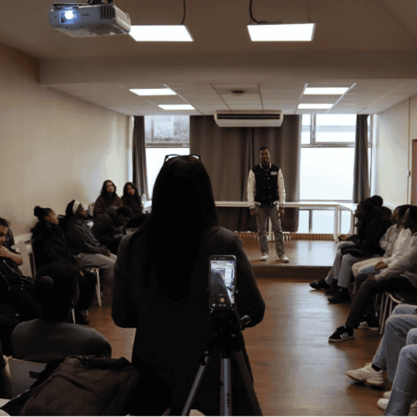 Sharing Week 2026 : à la découverte des métiers du commerce Un trépied avec un téléphone est au premier plan et filme une intervenante de dos et en arrière plan un étudiant sur une estrade. D'autres étudiants sont assis de chaque côté